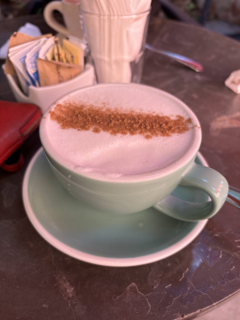 Green coffee cup with coffee topped with foamy milk and a line of brown turbinado sugar.